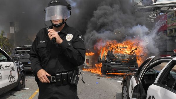 Полицейский Лос-Анджелеса на фоне горящей машины во время протестов  - Sputnik Молдова