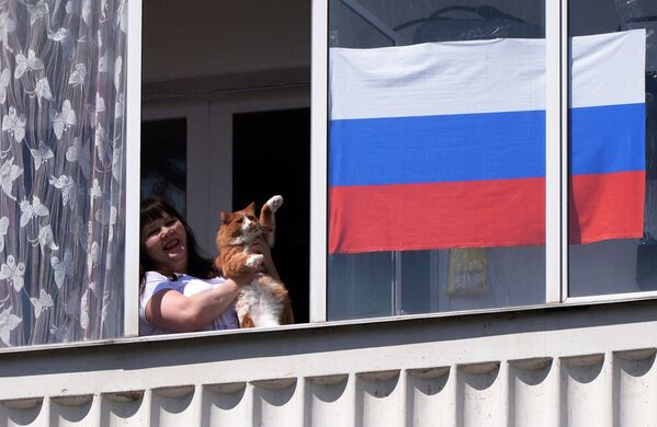 Жительница Красноярска со своим котом смотрит выступление музыкального ансамбля в День России из окна своей квартиры - Sputnik Молдова