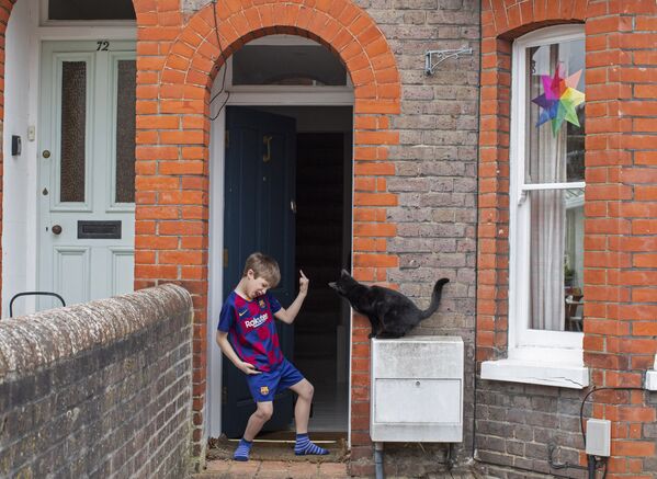 Юный футболист на пороге своего дома и соседский кот, заглядывающий через дверь, Великобритания - Sputnik Moldova