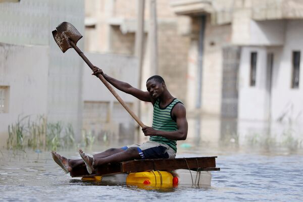 Житель на самодельном плоту с лопатой плывет по затопленным после проливных дождей улицам в Кеур-Массаре, Сенегал - Sputnik Молдова