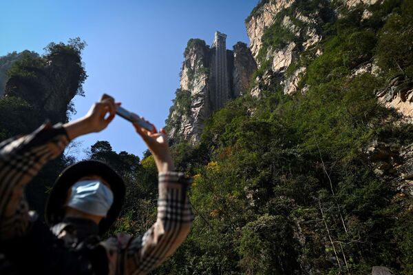 A tourist with a face mask takes a picture with her mobile phone at the entrance of the Bailong Elevator in the Zhangjiajie National Forest Park in China's Hunan province. - Sputnik Moldova-România