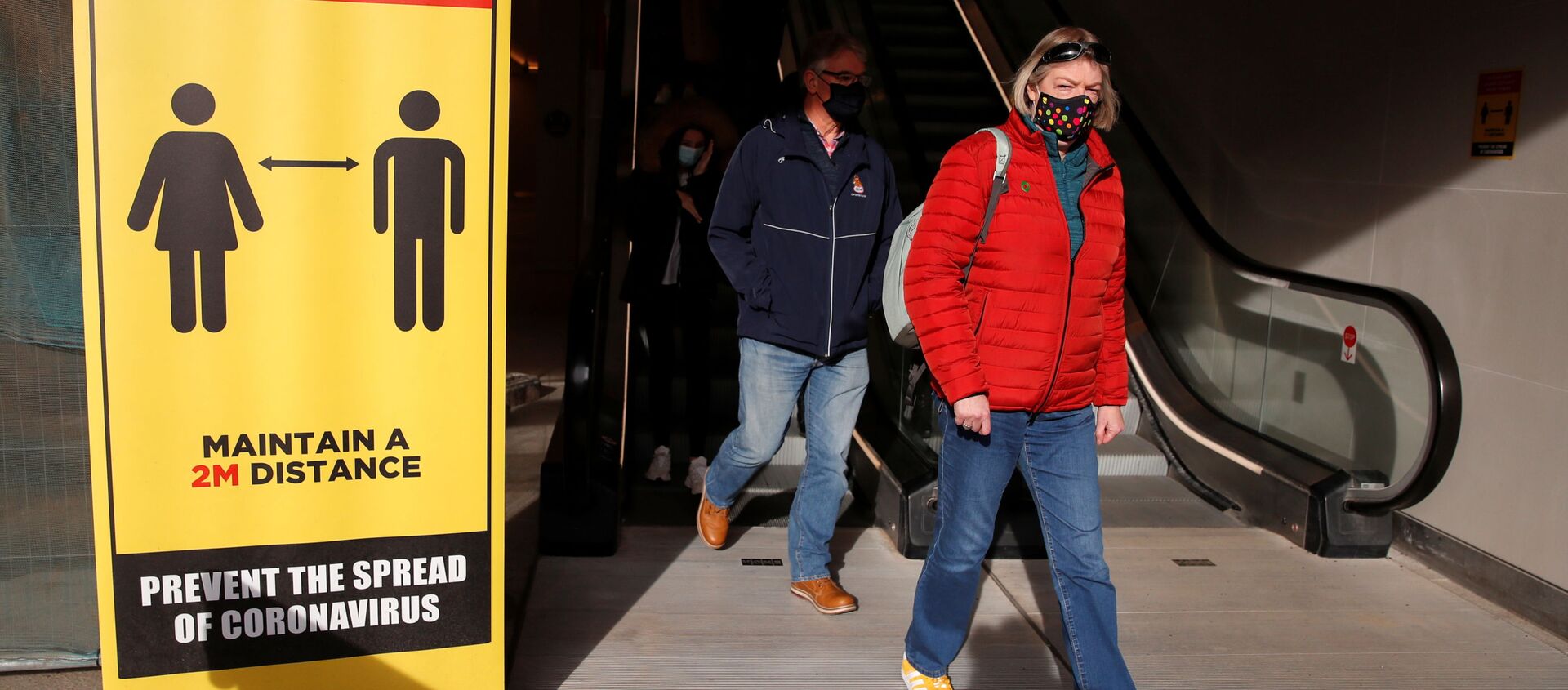 Люди в защитных масках проходят мимо знака социального дистанцирования в Ковентри, Великобритания - Sputnik Молдова, 1920, 26.11.2020