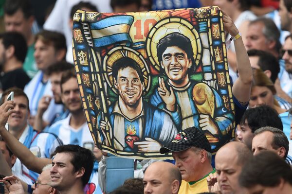 Болельщик Аргентины держит изображение нападающего Аргентины Лионеля Месси и бывшего футболиста Диего Марадоны в образе Святых перед футбольным матчем на стадионе Бейра-Рио в Порту-Алегри - Sputnik Молдова