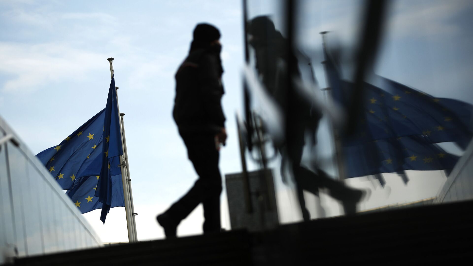 Пешеход идет под флагами ЕС у штаб-квартиры ЕС в Брюсселе - Sputnik Moldova-România, 1920, 03.10.2021