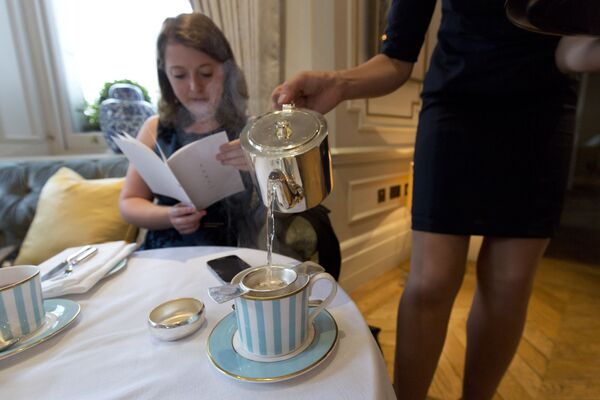 Сотрудница отеля наливает женщине чашку чая в отеле Kensington в Лондоне - Sputnik Moldova