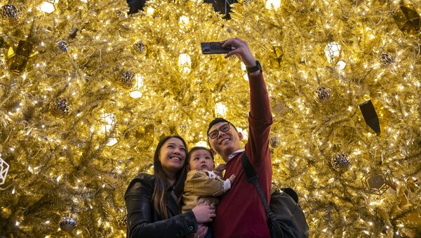 Молодые люди с ребенком фотографируются перед золотыми рождественскими елками в торговом центре в Гонконге - Sputnik Молдова