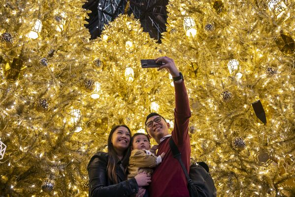 Молодые люди с ребенком фотографируются перед Золотыми рождественскими елками в торговом центре в Гонконге - Sputnik Молдова