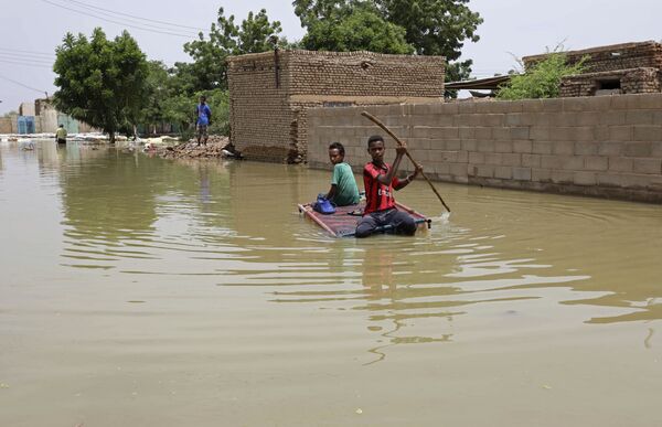 Подростки плывут на плоту по затопленной в результате наводнения улице в городе Салмания, Судан - Sputnik Moldova-România