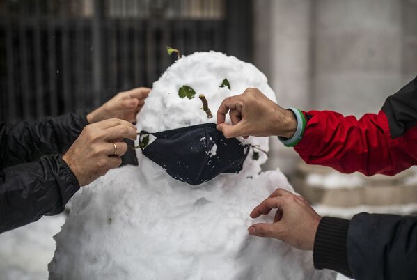 Oameni ce îi pun o mască unui om de zăpadă pe una din străzile Madridului - Sputnik Moldova-România