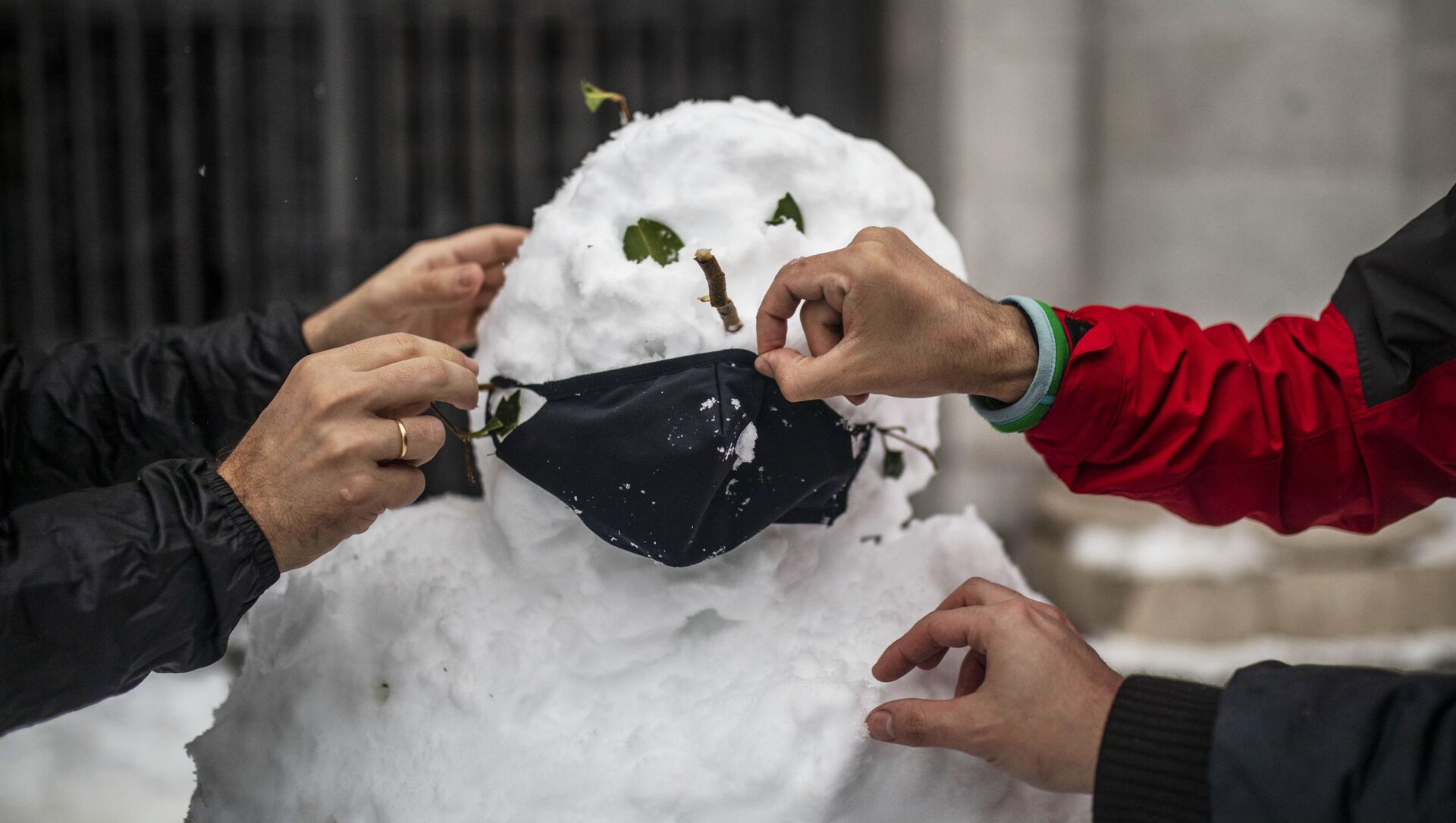 Люди надевают маску на слепленного снеговика на одной из улиц в Мадриде - Sputnik Молдова, 1920, 07.02.2021