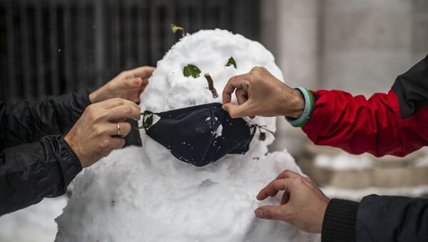 Люди надевают маску на слепленного снеговика на одной из улиц в Мадриде - Sputnik Молдова
