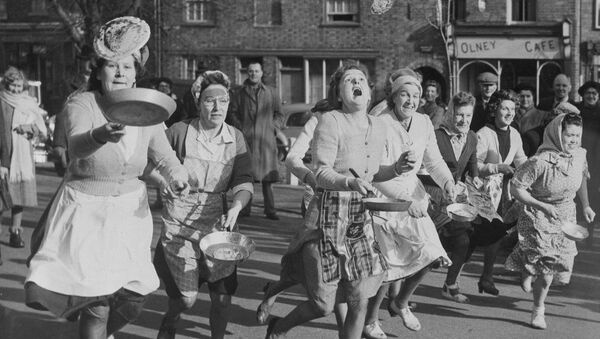 Gospodinele britanice aruncă clătite în tigaie în timp ce aleargă pe străzile din Olney, Anglia, în cursa anuală a comunității care urmează o tradiție veche de 500 de ani, 6 februarie 1951. - Sputnik Moldova