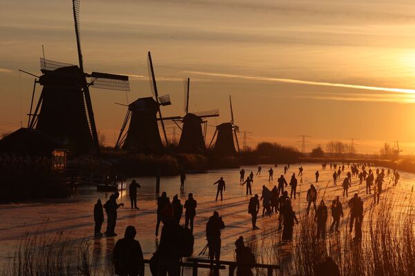 Люди катаются на коньках по замерзшему льду у ветряных мельниц в деревне Киндердейк, Нидерланды - Sputnik Молдова