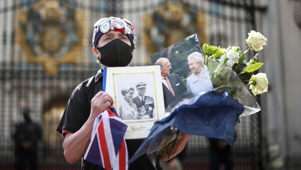 Скорбящий держит цветы и фотографии королевы Великобритании Елизаветы II и ее мужа принца Филиппа возле Букингемского дворца  - Sputnik Молдова