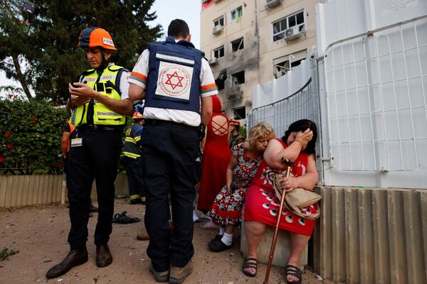 Израильские медики стоят рядом с женщинами возле дома, поврежденного ракетой, запущенной из сектора Газа в Ашкелоне - Sputnik Moldova-România