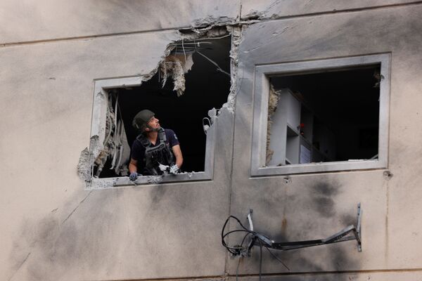 Эксперт по обезвреживанию бомб израильской полиции смотрит из окна жилого дома, который был поврежден после попадания в него ракеты, запущенной из сектора Газа, в Ашкелоне - Sputnik Moldova-România