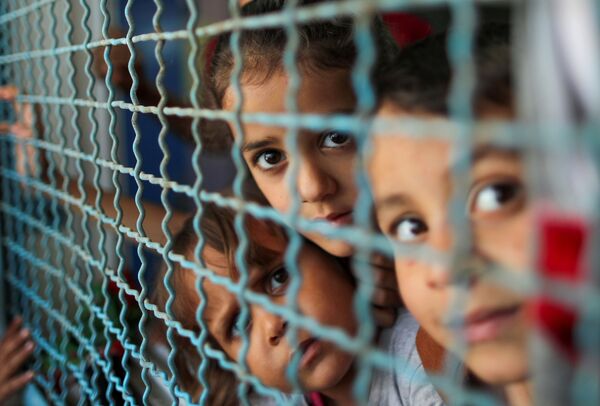 Палестинские дети, покинувшие свои дома из-за израильских воздушных и артиллерийских ударов, смотрят через оконное ограждение школы, управляемой Организацией Объединенных Наций, в которой они укрываются, в городе Газа  - Sputnik Молдова