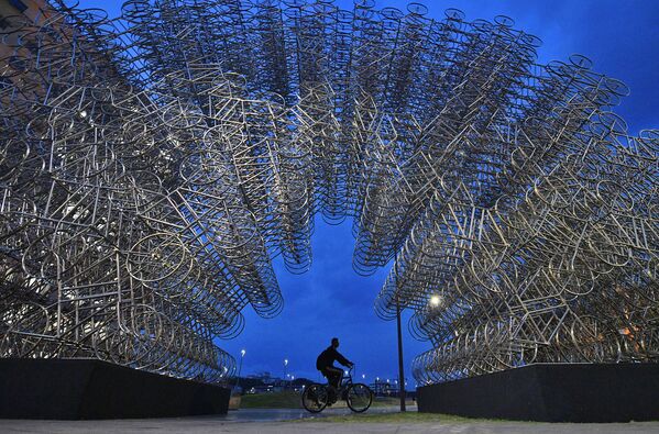 Un bărbat merge cu bicicleta pe lângă o instalație de artă intitulată „Forever Cycles” a artistului chinez Ai Weiwei din Rio de Janeiro, Brazilia, pe 19 august 2019. - Instalația este alcătuită din peste 1000 de biciclete din oțel inoxidabil și face parte din expoziția lui Ai Weiwei , care se deschide la Rio de Janeiro pe 21 august 2019. - Sputnik Moldova-România