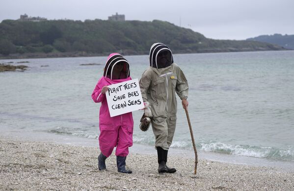 Activiștii climatici Delores și Leroy Tyclemore poartă costume de apicultori în timpul unei demonstrații pe plaja Gillingves din Falmouth, Cornwall, Anglia - Sputnik Moldova