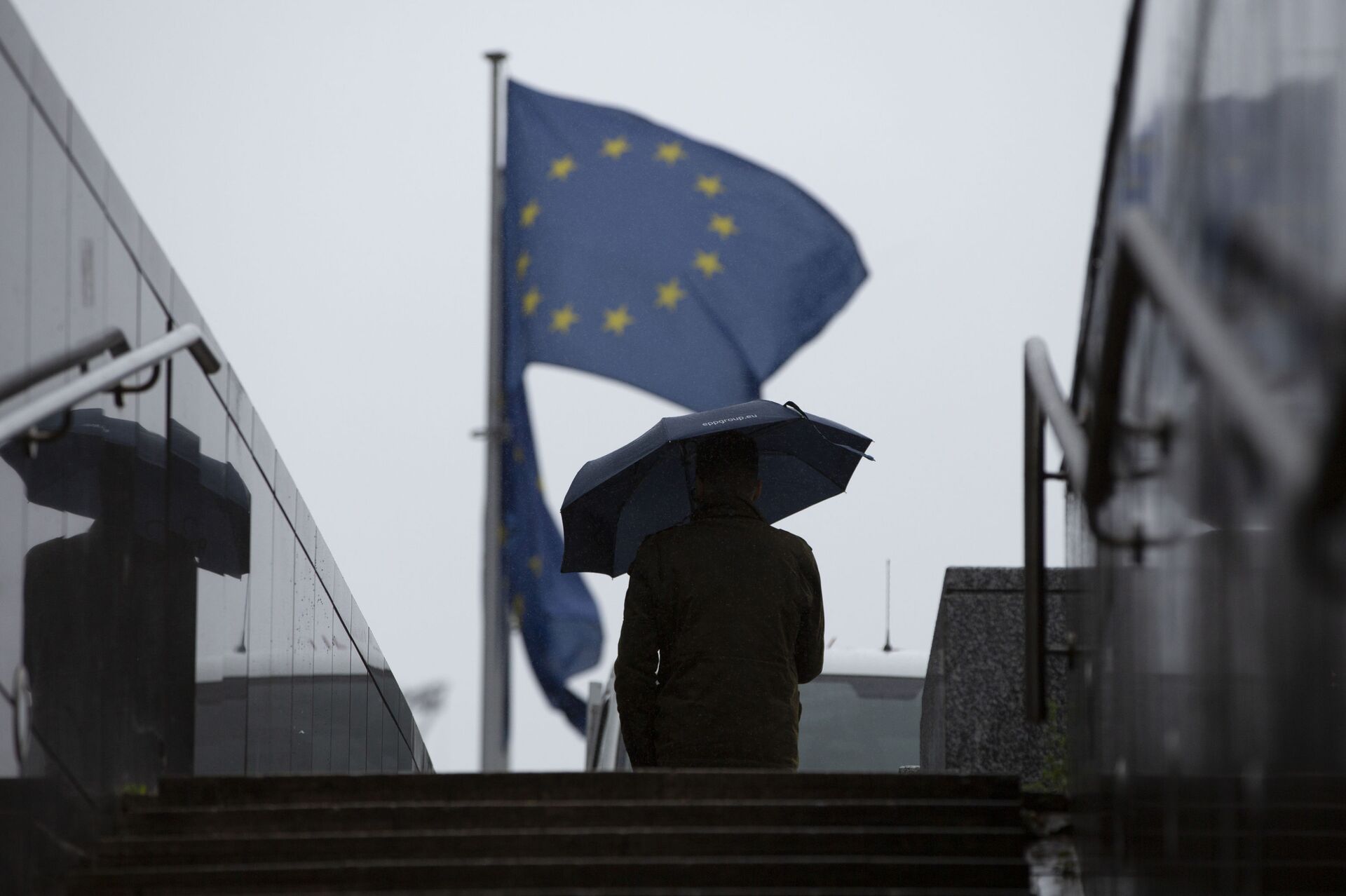 Мужчина с зонтиком идет к флагам ЕС у штаб-квартиры ЕС в Брюсселе - Sputnik Молдова, 1920, 20.07.2021