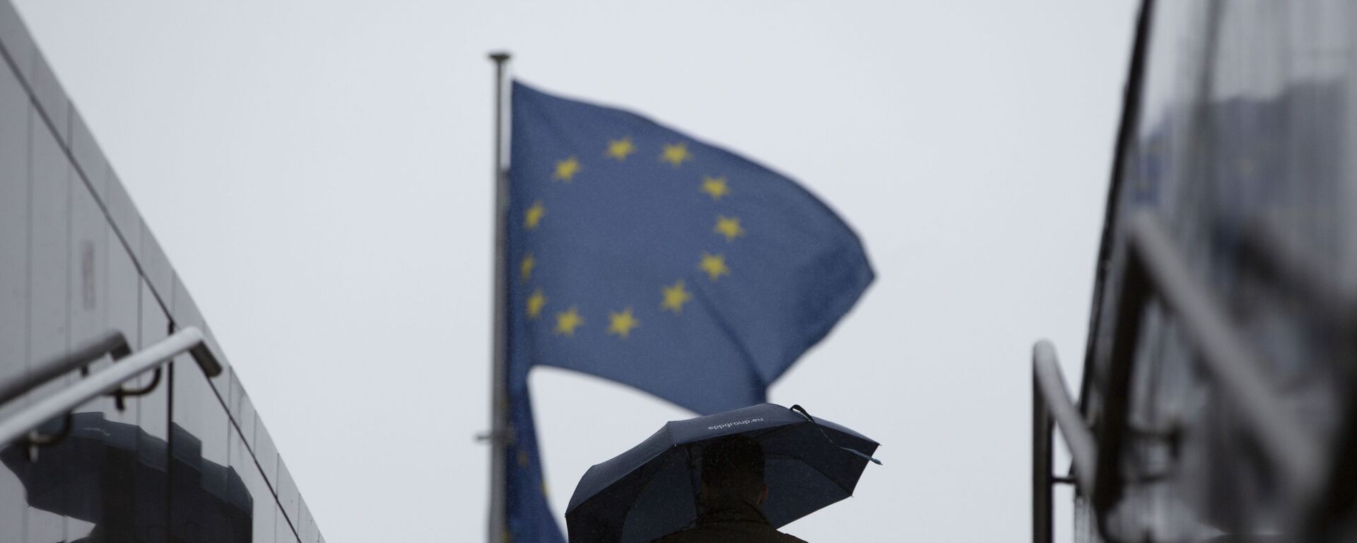 Мужчина с зонтиком идет к флагам ЕС у штаб-квартиры ЕС в Брюсселе - Sputnik Молдова, 1920, 25.06.2021