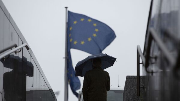 Мужчина с зонтиком идет к флагам ЕС у штаб-квартиры ЕС в Брюсселе - Sputnik Молдова