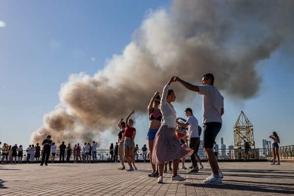 Пары танцуют самбу, в то время как над горящим складом пиротехники поднимается дым, Москва. - Sputnik Молдова