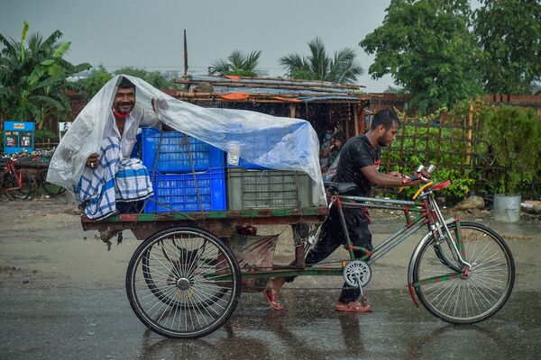 Мужчина укрывается от дождя, сидя на тележке велорикши во время ливня в Дакке. - Sputnik Молдова