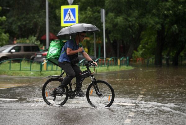 Un bărbat pe bicicletă pe o stradă din Moscova în timpul ploii puternice de luni. - Sputnik Moldova