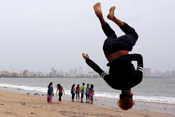 Oamenii se plimbă în timp ce un băiat face o acrobație pe plaja din Mumbai, India. - Sputnik Moldova