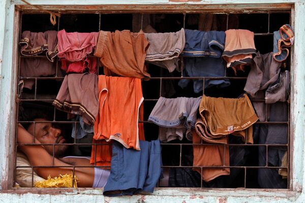 Обитатель трущоб спит у окна, завешанного бельем сушиться, в лачуге в Дхарави, Мумбаи. - Sputnik Молдова