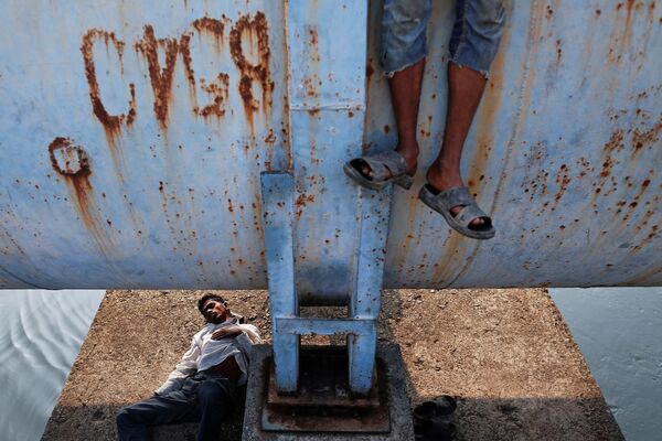 Мужчина спит под водопроводом, в то время как другой стоит на нем в Мумбаи. - Sputnik Молдова