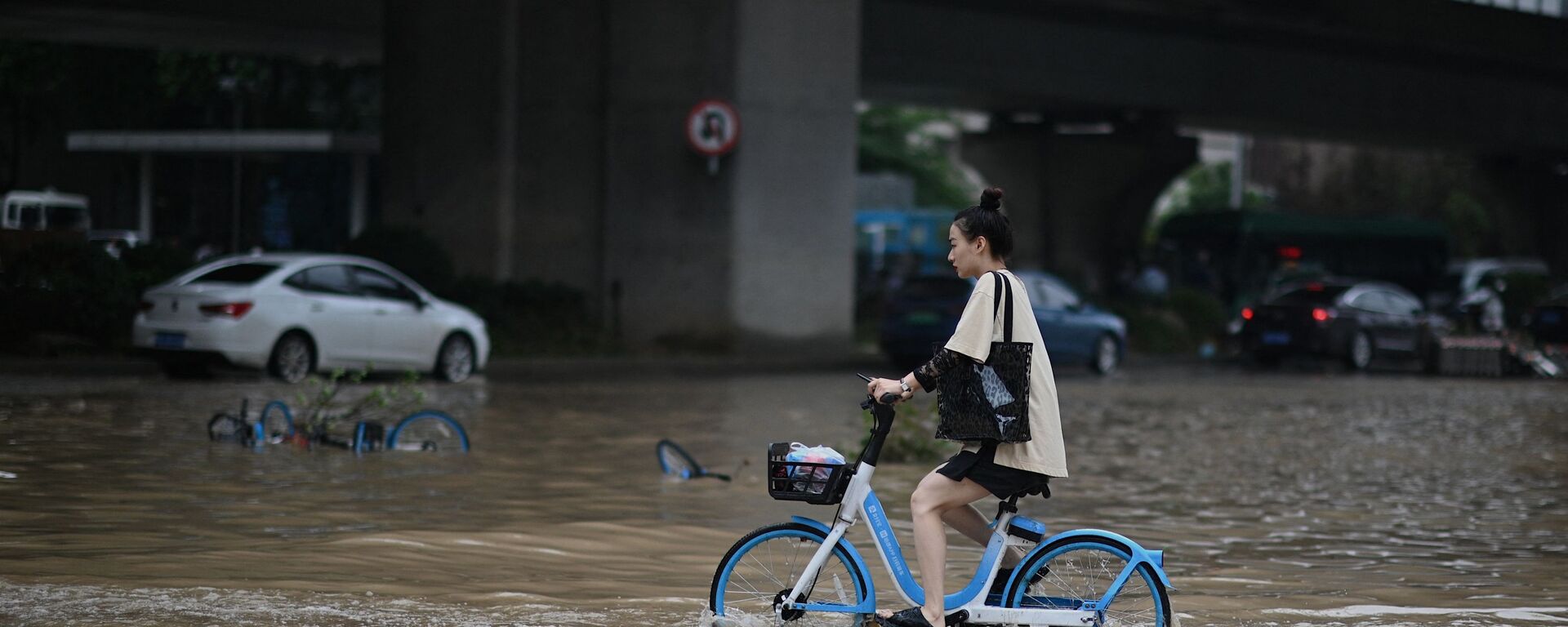 Девушка едет на велосипеде на затопленной улице в китайской провинции Хэнань  - Sputnik Молдова, 1920, 13.08.2021