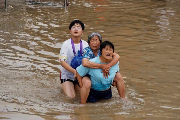 O femeie duce o femeie în vârstă în timp ce își croiește drum prin apele inundațiilor în urma precipitațiilor abundente din Zhengzhou, provincia Henan, China, 23 iulie 2021. - Sputnik Moldova-România