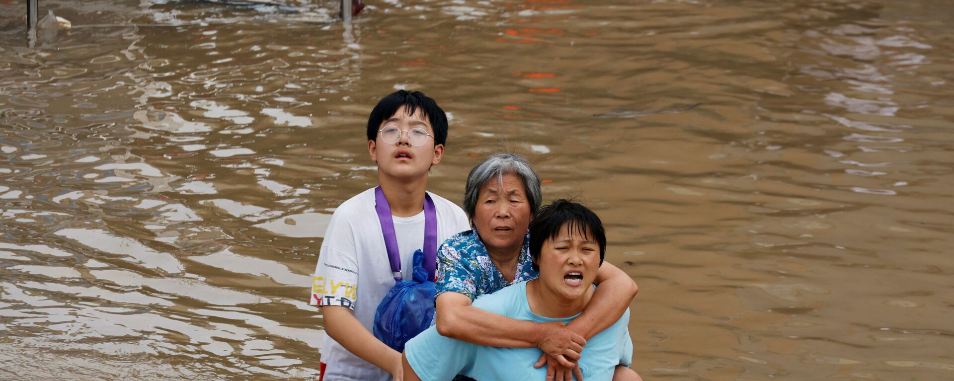 Женщина несет пожилую женщину  через паводковые воды после проливного дождя в Чжэнчжоу, провинция Хэнань, Китай - Sputnik Moldova-România, 1920, 26.07.2021