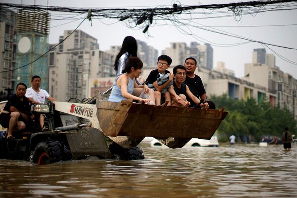 Oamenii se deplasează pe un încărcător frontal în timp ce își croiesc drum prin apele inundațiilor în urma precipitațiilor abundente din Zhengzhou, provincia Henan, China, 23 iulie 2021. - Sputnik Moldova-România