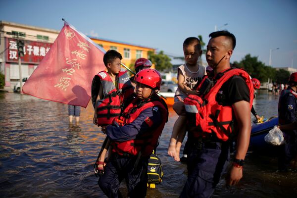 Membrii echipei Dawn Emergency Rescue țin copii în brațe în timp ce evacuau sătenii blocați de apele inundațiilor în urma precipitațiilor abundente într-un sat din Xinxiang, provincia Henan, China, 24 iulie 2021. - Sputnik Moldova-România