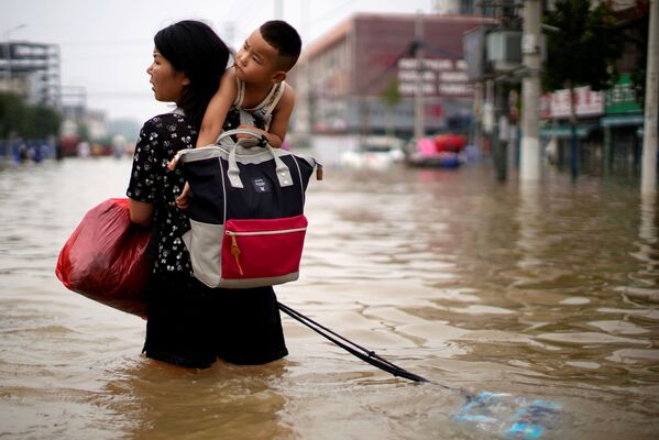 O femeie care duce un copil pătrunde prin apele inundațiilor în urma precipitațiilor abundente din Zhengzhou, provincia Henan, China, 23 iulie 2021. - Sputnik Moldova-România