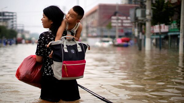 Женщина с ребенком и вещами пробирается через паводковые воды после проливного дождя в Чжэнчжоу, провинция Хэнань, Китай - Sputnik Молдова
