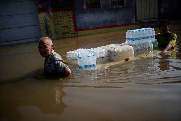 Sătenii care transportă sticle de apă rătăcesc prin apele inundațiilor după precipitațiile abundente într-un sat din Xinxiang, provincia Henan, China, 24 iulie 2021. - Sputnik Moldova-România