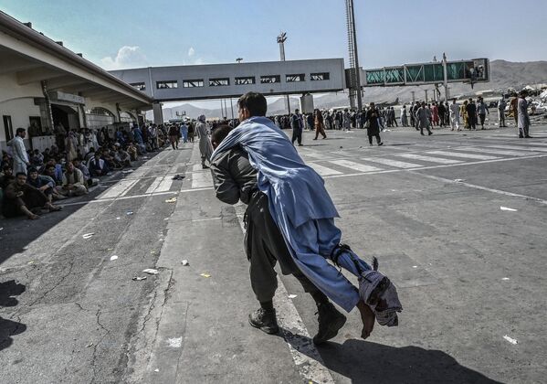 Un voluntar transportă un bărbat rănit, în timp ce alte persoane își așteaptă plecarea din aeroportul din Kabul din Kabul pe 16 august 2021 - Sputnik Moldova-România