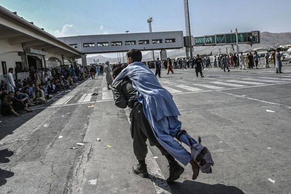 Волонтер несет раненого мужчину, пока другие люди ждут в аэропорту Кабула в Кабуле. - Sputnik Молдова