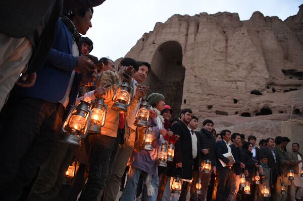 Locuitorii și activiștii societății civile dețin lămpi în timp ce stau în apropierea locului în care statuia lui Buddha Salsal a stat cândva în timpul unei ceremonii de comemorare a 20 de ani de la distrugerea Buddha a statuilor Bamiyan de către talibani în martie 2001, în provincia Bamiyan, pe 9 martie 2021. - Sputnik Moldova-România