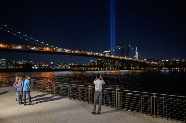 Oamenii fac fotografii de pe malul apei din Brooklyn cu o instalație de lumină intitulată „Tribut în lumină” care comemorează atentatele teroriste din 11 septembrie, la New York, pe 10 septembrie 2021. - Sputnik Moldova-România