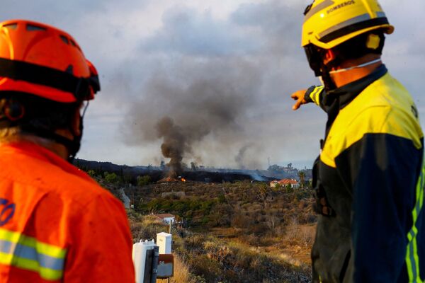 Un membru al Protecției Civile și un pompier forestier privesc cum o casă arde din cauza lavei din erupția unui vulcan din parcul național Cumbre Vieja, în zona rezidențială Los Campitos la Los Llanos de Aridane, pe Insula Canare La Palma , 20 septembrie 2021. - Sputnik Moldova-România
