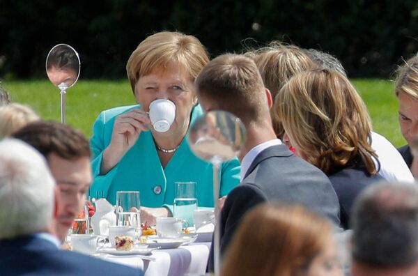 Cancelarul german Angela Merkel bea cafea în timp ce participă la un eveniment de „masă de cafea” găzduit de președintele german pentru a sărbători cea de-a 70-a aniversare a Constituției (Grundgesetz) în grădina Palatului prezidențial Bellevue din Berlin pe 23 mai 2019. - Sputnik Moldova-România