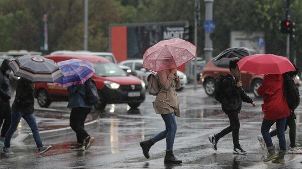 Trecatori cu umbrele traverseaza Calea Victoriei in timpul unui cod galben de vreme rea pentru vant, ploaie si instabilitate atmosferica, in Bucuresti - Sputnik Moldova-România