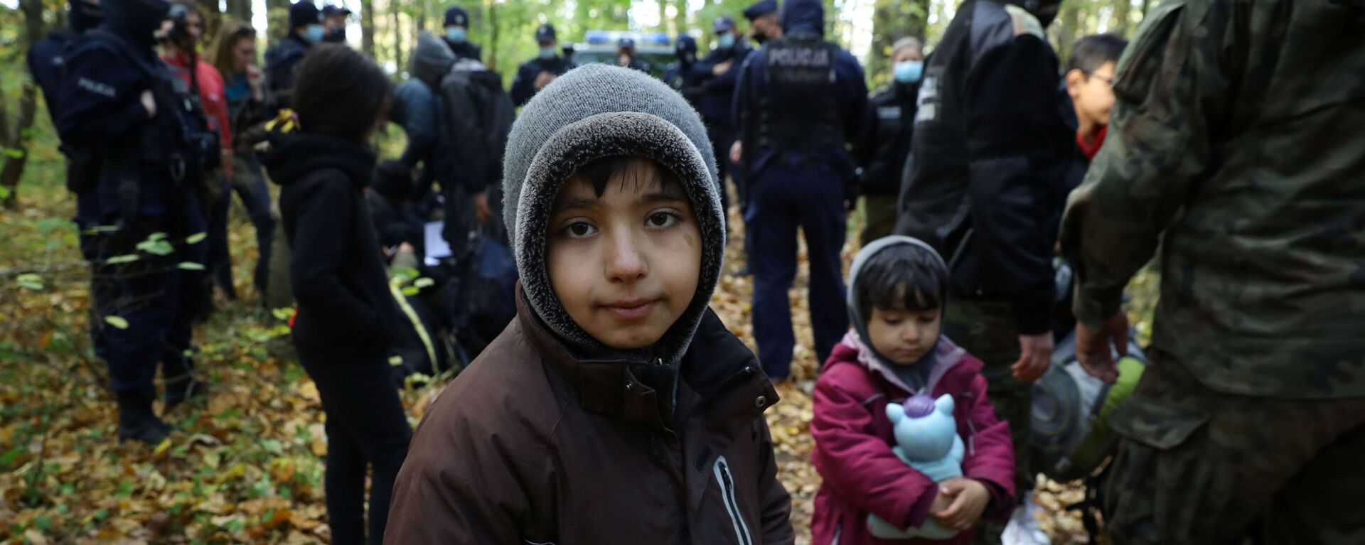 Иракский ребенок в окружении пограничников и полицейских после пересечения белорусско-польской границы в городе Хайнувка, Польша - Sputnik Moldova-România, 1920, 16.10.2021