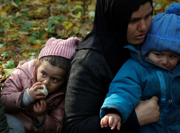 O femeie migrantă irakiană cu copii stă pe pământ, în timp ce este înconjurată de polițiști de frontieră și ofițeri de poliție după ce au trecut frontiera bielorusă-poloneză în timpul crizei imigranților în curs, în Hajnowka, Polonia, 14 octombrie 2021. - Sputnik Moldova-România