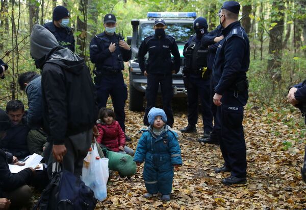 Un copil migrant irakian stă în picioare în timp ce el și alții sunt înconjurați de polițiști de frontieră și ofițeri de poliție după ce au trecut frontiera bielorusă-poloneză în timpul crizei imigranților în curs, în Hajnowka, Polonia, 14 octombrie 2021. - Sputnik Moldova-România